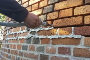 Une main applique du mortier entre les briques d’un mur à l’aide d’un pistolet à tuyau