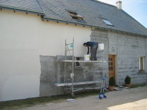 Un homme travaille sur l’enduit extérieur d’une maison depuis un échafaudage