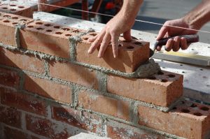 Un maçon pose une brique sur un mur en construction à l’aide d’un mortier