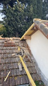 Toiture en tuiles anciennes en cours de rénovation, avec gravats et planches autour d’un avant-toit